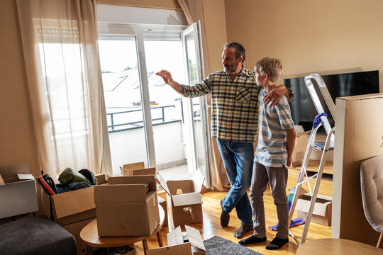 A father and son are unpacking boxes and moving into their new home. They carry items, arrange furniture, and help each other settle into the space.