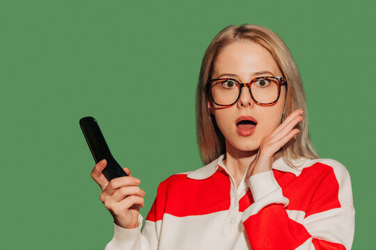 Surprised woman with glasses holding a flip phone in a red striped jacket
