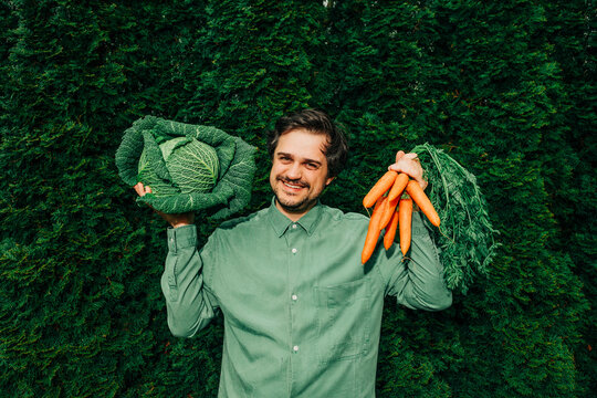 Man in green shirt holding carrots and Italian kale outdoors