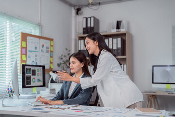 Two asian businesswomen analyzing financial charts on a computer, working together in a modern...