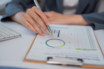 Businesswoman analyzing financial charts and graphs using pen and keyboard, focusing on market trends and investment strategies for maximum profitability