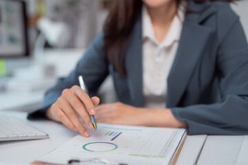 Businesswoman pointing at financial charts and graphs using pen while working on performance,...