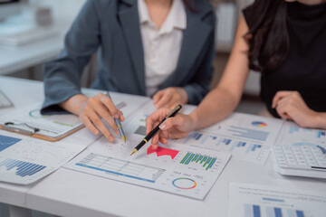 Two businesswomen are pointing at financial charts and graphs with pens while discussing company strategy and planning for future investments