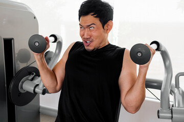 Focused Asian man lifting dumbbells with intense facial expression