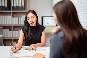 Two businesswomen discussing financial charts at an office desk, analyzing data and reports while...