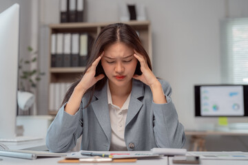Young Asian businesswoman experiencing a headache while reviewing financial graphs and charts at...