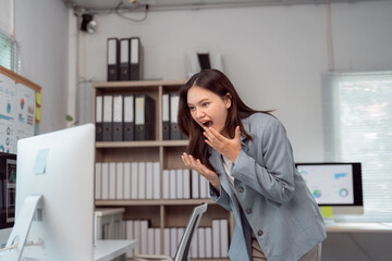 Young businesswoman is standing in her office, looking at her desktop computer with a surprised expression, her hand covering her mouth in amazement