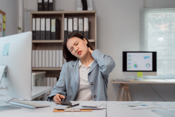 Young businesswoman massaging her neck to relieve tension while calculating financial reports in...