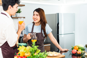 Young couple cooking healthy food together in a bright kitchen, smiling and enjoying fresh juice surrounded by fruits and vegetables. Perfect image for healthy living, love, and home cooking themes.