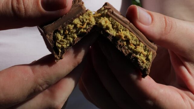 Breaking a Piece of Dubai Chocolate Bar in Hands with Crispy Filling, Sweet Snack Texture Concept