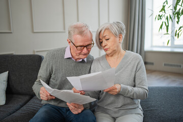 Sad tired disappointed middle aged senior couple sit with paper document. Unhappy older mature man woman reading paper bill managing bank finances calculating taxes planning loan debt pension payment