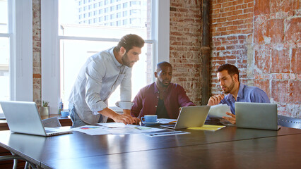 Multi-Cultural Group Of Businessmen Working Together Using Laptops In Boardroom