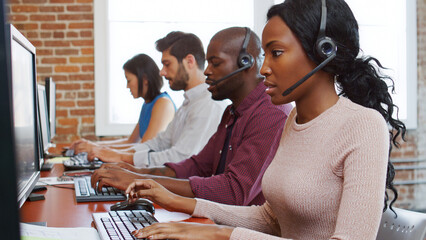 Multi-Cultural Business Team Wearing Headsets Working In Busy Customer Service Department