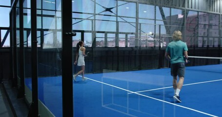 Diverse athletes playing padel tennis on blue indoor court, focusing on teamwork