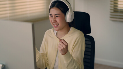 Joyful Asian woman celebrating success with a smile during online meeting at home. Wearing...