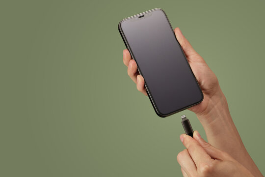 female hand connect charger cord into smartphone to charge battery isolated on green background, Wired charging