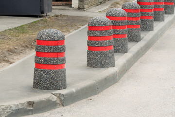 Concrete bollards with bright red stripes line urban sidewalk, creating visual rhythm and enhancing...
