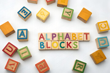 Obraz premium Scattered colorful wooden alphabet blocks arranged on a clean white background. Great for educational content, children's design, and playful branding.