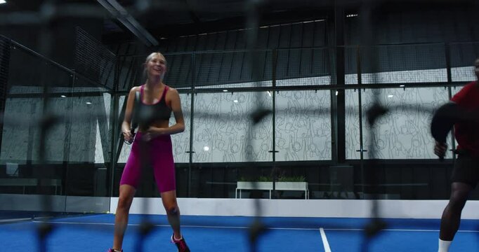 Playing padel tennis, woman in pink outfit hitting ball on blue indoor court