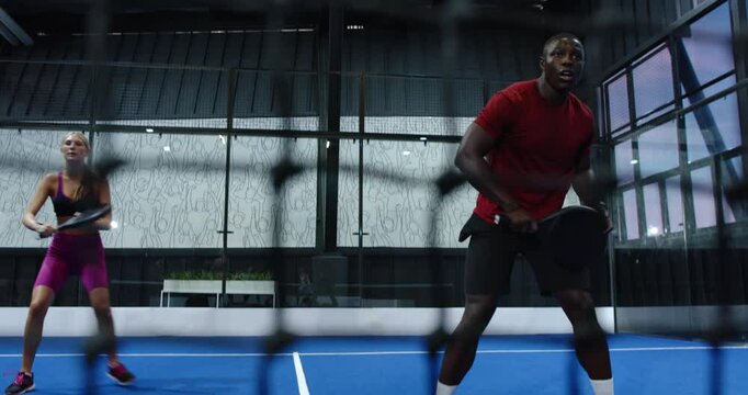 Playing padel tennis on indoor court, two athletes practicing on blue indoor court