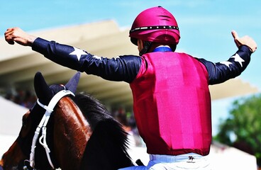 Jockey de espaldas celebrando victoria sobre caballo de carreras con los brazos abiertos y pulgar arriba en el hipódromo 