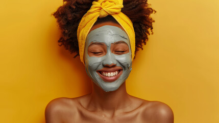 happy african american woman wearing a mud clay face mask on a yellow background, female skincare pampering regimen
