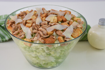 Classic Chicken Caesar Salad in a clear glass bowl with crisp lettuce, tender grilled chicken pieces, croutons, and Parmesan cheese with napkin closeup side view of refreshing salad