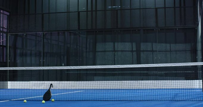 Padel tennis racket and balls on blue indoor court near net, ready for play, copy space