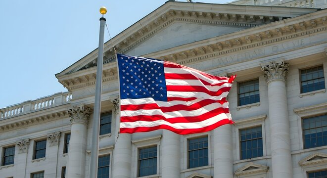A large American flag flies in the blue sky in front of a colonnaded building. - Powered by Adobe