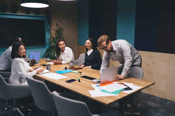 Diverse business team listening carefully during formal team discussion in boardroom, focused on company strategy with documents, laptops, and digital tools laid out for review