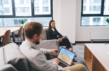 Team meeting blends focus and collaboration as professionals chat on couch and others brainstorm at...