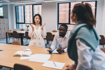 Asian businesswoman explaining idea to multicultural team during informal meeting in bright open office, promoting communication, leadership, and collaborative team culture