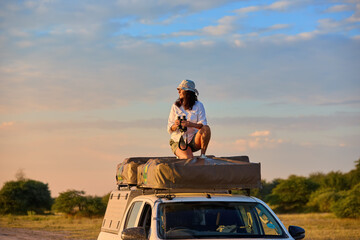 Woman on roof of the safari car looking for animals. Self-Drive Safari in Nxai Pan, Botswana at Golden Hour.