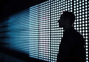 Silhouette of a man standing near illuminated neon LED wall. Concept of futuristic cyberspace,  metaverse, modern digital technology. 