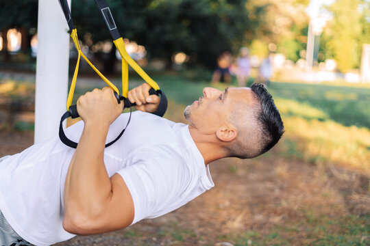 Sportsman using trx fitness straps when performing chin-ups - Powered by Adobe