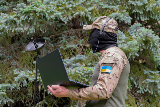 A military man in camouflage with a Ukrainian flag uses a directional microphone and a laptop in the forest, conducting radio reconnaissance. - Powered by Adobe