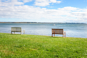 Empty wooden benches on grass facing a bay along the coast of Connecticut on a sunny autumn morning