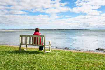 Woman sitting  on a wooden bench in front of a scenic  bay on  a sunny autumn morning