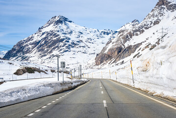 Empty winding road running alongside a railway through a snowy mountain pass in the Swiss Alps in early spring