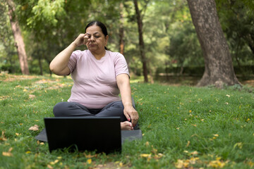 Indian female overweight in training exercise to lose weight on mat looking preview with laptop....
