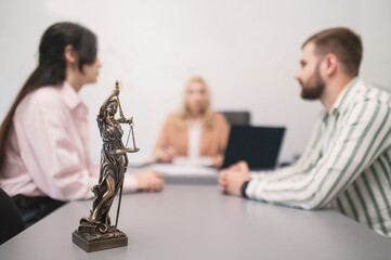 Married couple filing divorce papers in lawyer's office. Statue of Themis close-up in lawyer's...