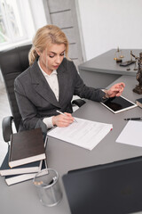 Professional woman in gray suit working with legal documents at office desk, Lady Justice scales...