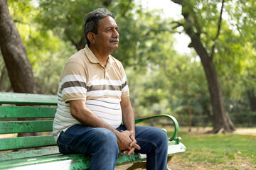 Depression, thinking, Upset lonely homeless senior man in garden sitting on bench with depression...
