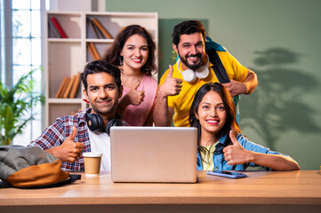 Using laptop, Indian students complete assignment and smile at camera showing thumbs up