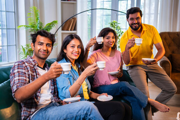 Happy Indian youth sipping chai and bonding on sofa in a cozy indoor home environment
