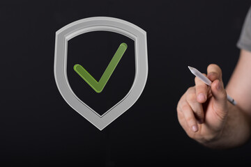 Stock photo of a hand drawing a check mark inside a shield, symbolizing data security and...