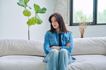 Sad upset young woman sitting on sofa at home