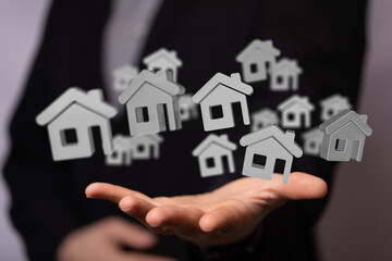 Image of a real estate agent's hand holding multiple digital house icons, representing property...