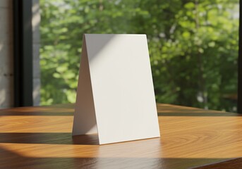 Blank white tent card on wood table in front of green foliage for messages