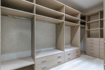 Spacious dressing room with beige furniture. Spacious cabinets with shelves and storage drawers.